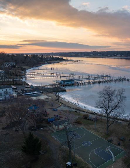 Aerial view of Little Silver, NJ at sunset, featuring waterfront marinas, docks extending into calm river waters, and a shoreline park overlooking the scenic Navesink River.