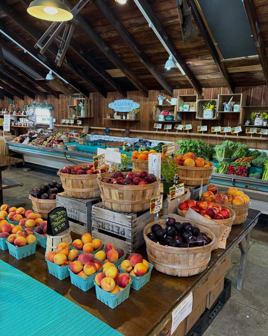 Local farm market near Mahwah, New Jersey, filled with baskets of fresh peaches, plums, leafy greens, vegetables, and other seasonal produce displayed inside a rustic wooden farm stand.