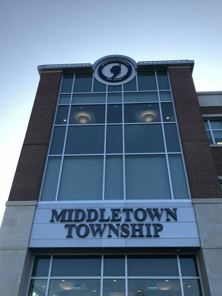 Exterior of the Middletown Township municipal building in Middletown, New Jersey, featuring a modern brick-and-glass facade, large township signage, and the official Middletown Township seal.