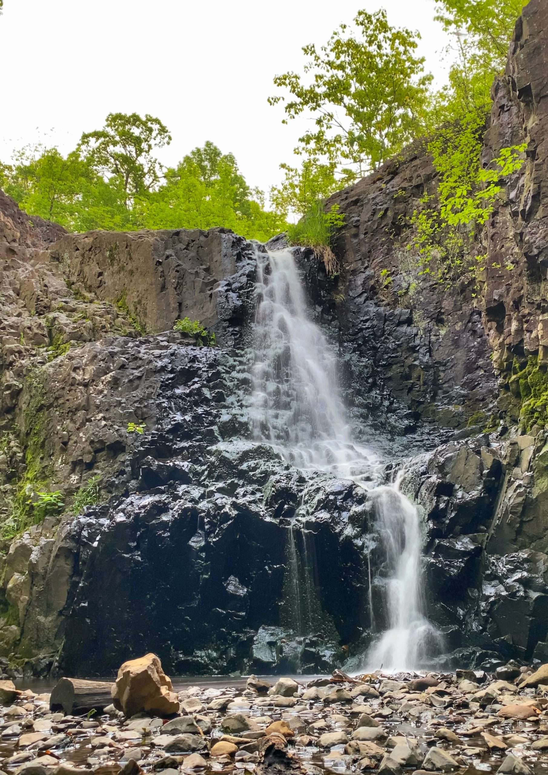 Waterfall cascading down rugged rock formations in Millburn, NJ, surrounded by lush greenery and a rocky streambed, creating a peaceful natural scene.
