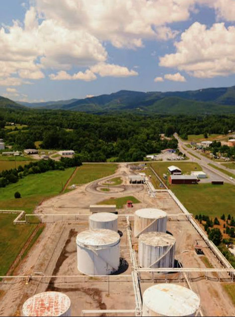 Elevated landscape view near Montvale, New Jersey, featuring an industrial facility with large storage tanks in the foreground and densely wooded hills and mountains stretching across the horizon.