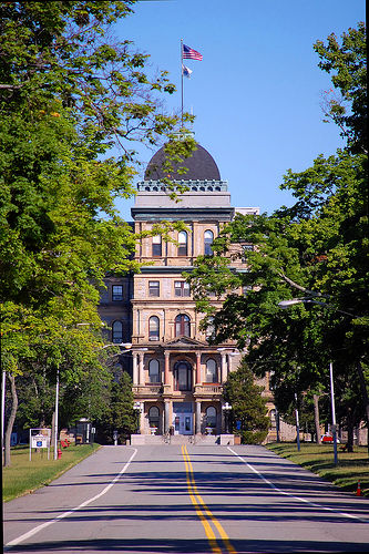 Historic Morris County government building in New Jersey, featuring ornate stone architecture, a domed roof and American flag, viewed from a tree-lined roadway leading toward the building.