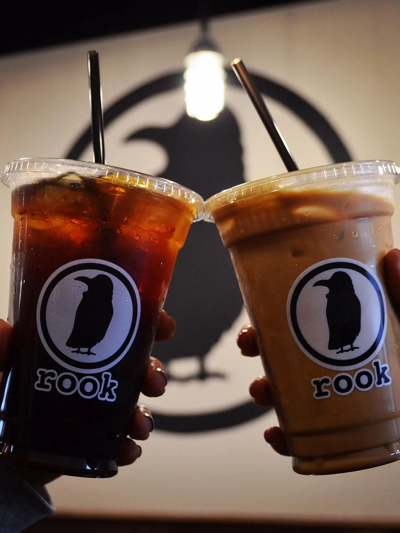 Two iced coffee drinks from Rook Coffee in Oakhurst, New Jersey, held in front of the coffee shop’s recognizable black bird logo.