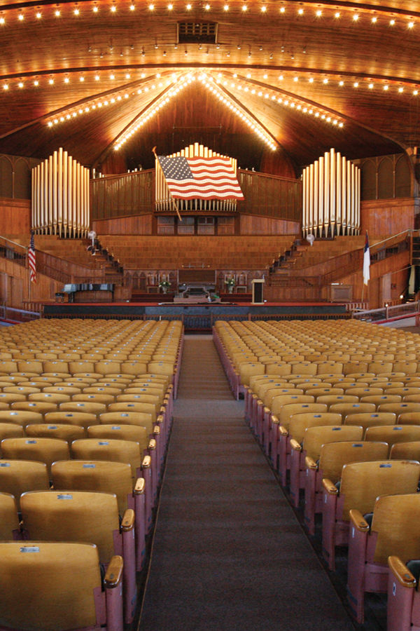 Interior of the historic Great Auditorium in Ocean Grove, New Jersey, featuring rows of seating, a large pipe organ, American flag, wooden architecture, and warm overhead lights.