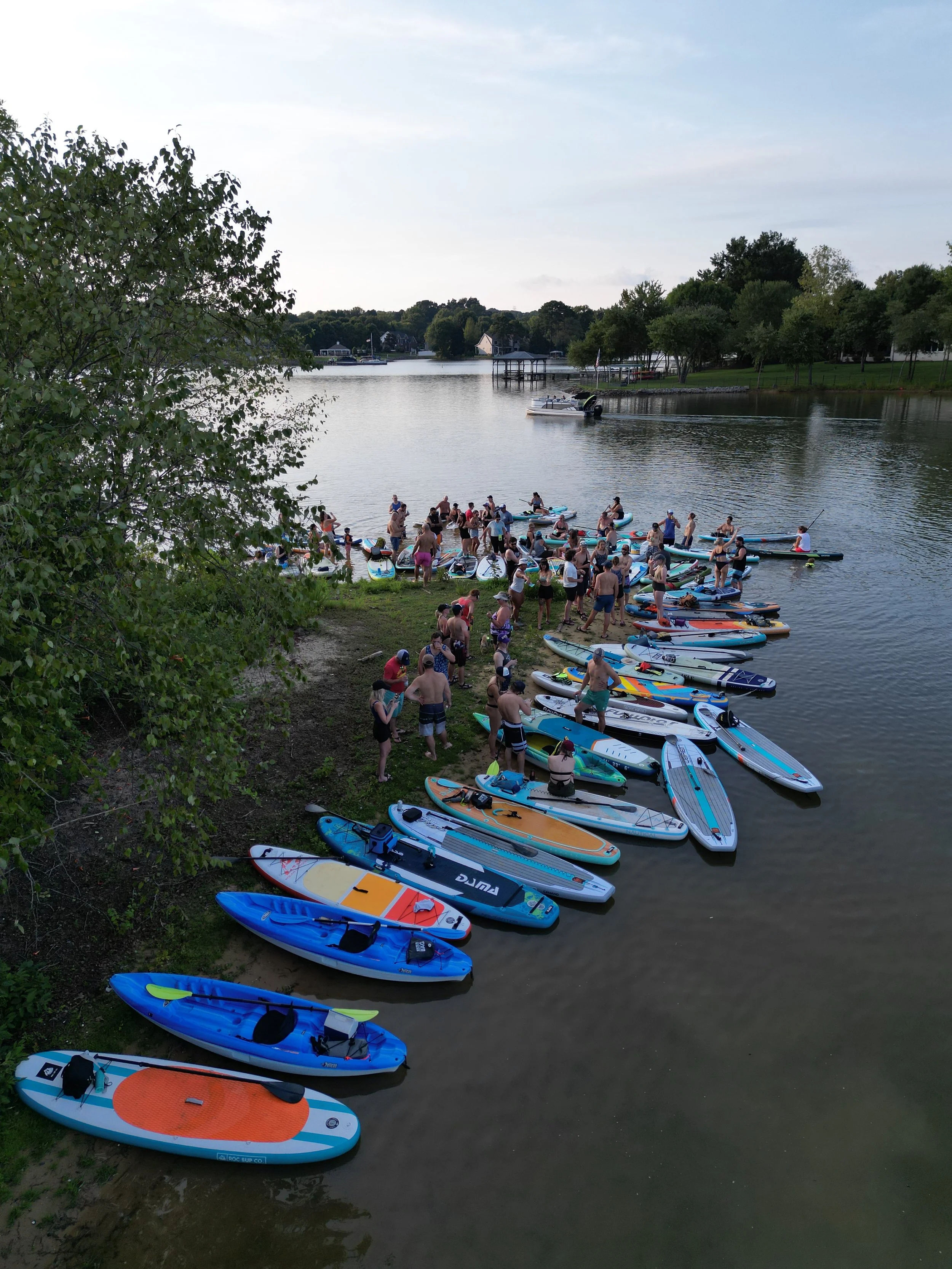 Large group of kayakers and paddleboarders gathered along the shoreline in Oceanport, New Jersey, with colorful paddleboards and kayaks covering the water’s edge.