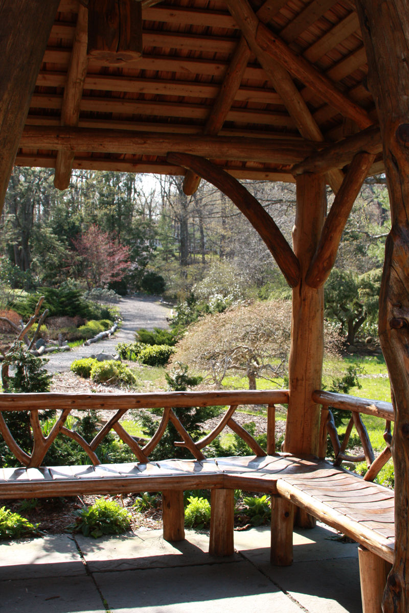Rustic wooden gazebo overlooking landscaped gardens and walking paths at Laurelwood Arboretum in Wayne, New Jersey, surrounded by trees, shrubs, and seasonal plantings.