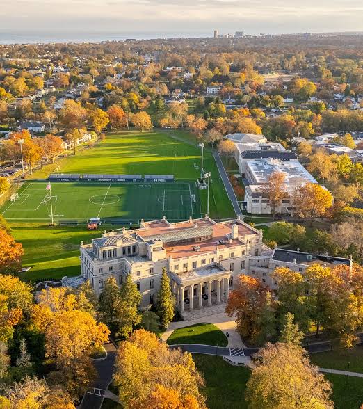 Aerial view of the Monmouth University campus in West Long Branch, New Jersey, featuring historic Wilson Hall, surrounding lawns, athletic fields, campus buildings, and colorful autumn trees.