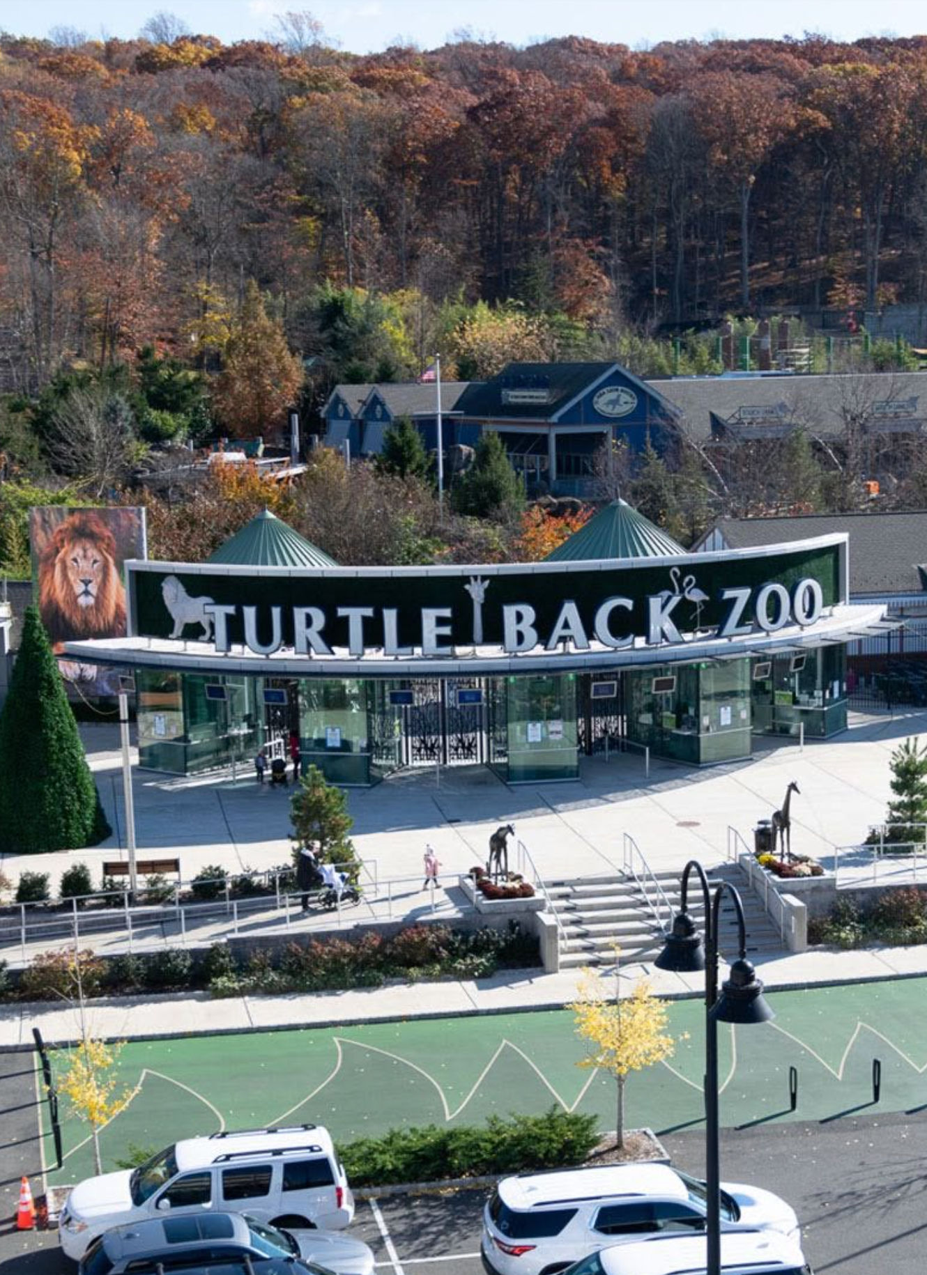 The entrance to Turtle Back Zoo in West Orange, New Jersey, with the main gateway, visitor plaza, and surrounding wooded hills.