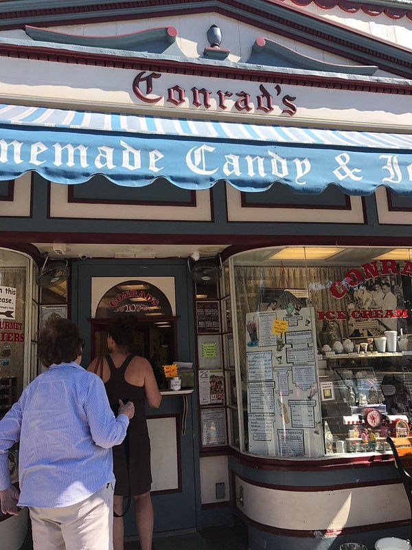 Exterior of Conrad's Confectionery in Westwood, New Jersey, a longtime local candy and ice cream shop, featuring its vintage storefront, striped awning, service window, and customers outside.