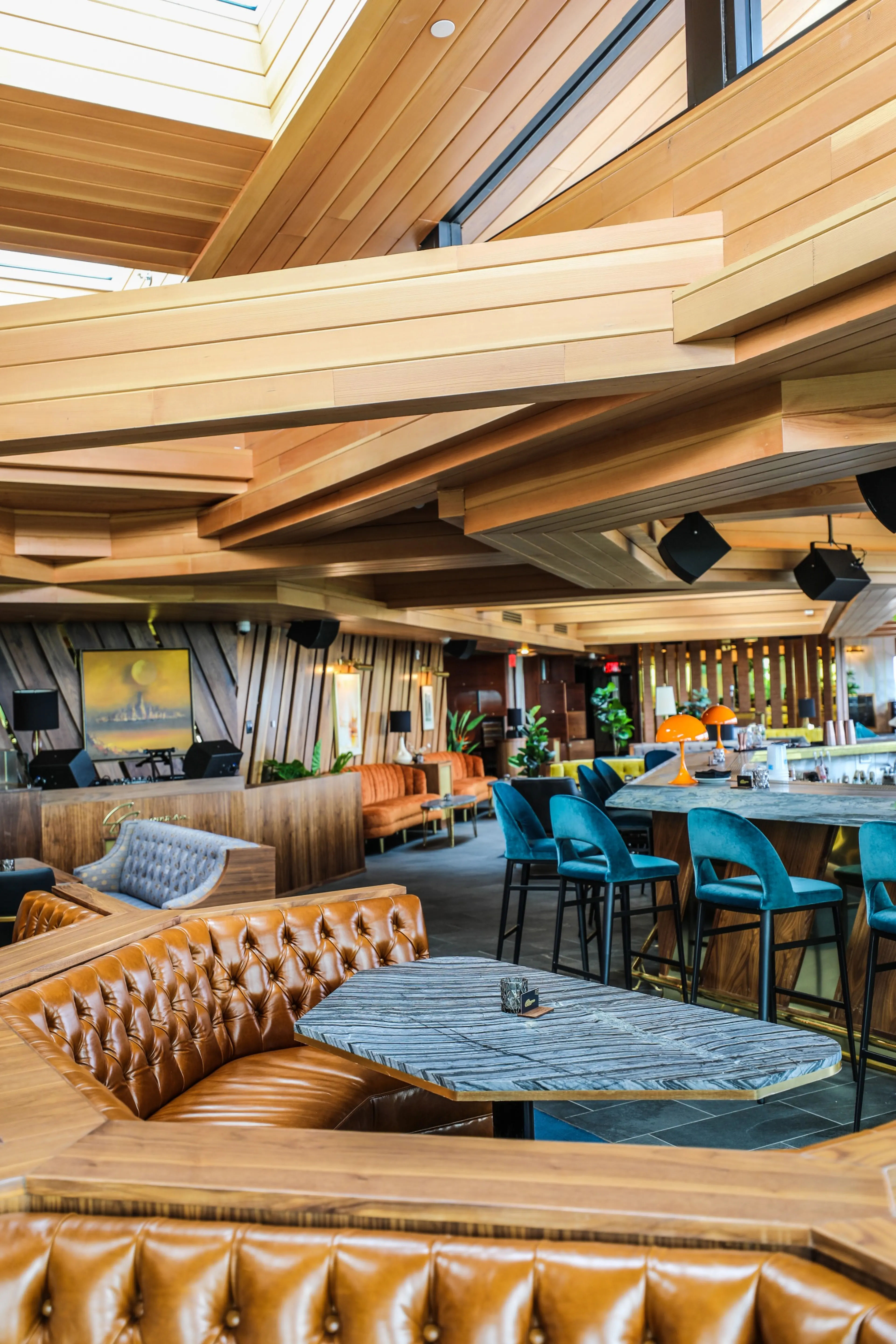 Modern dining and bar interior near Wood-Ridge, New Jersey, featuring tufted leather booths, marble-top tables, teal bar stools, warm wood architectural details, contemporary lighting, and lounge-style seating.