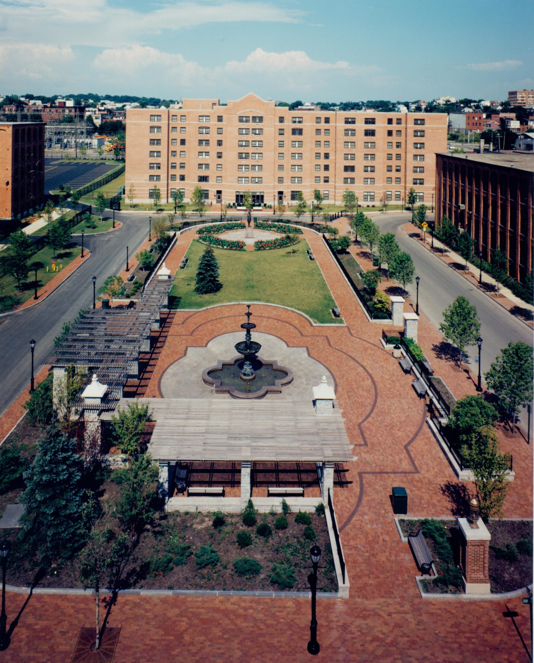 Aerial view of a landscaped public plaza in Franklin Square, New York, featuring brick walkways, fountains, green spaces, and surrounding residential buildings.