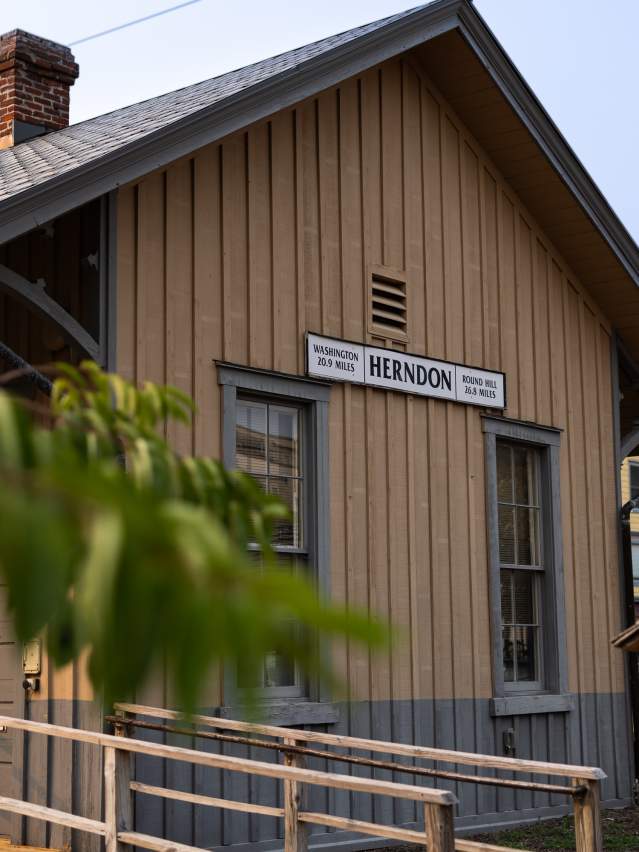 Historic Herndon, VA train depot building featuring wooden siding and a vintage station sign marking distances to Washington and Round Hill