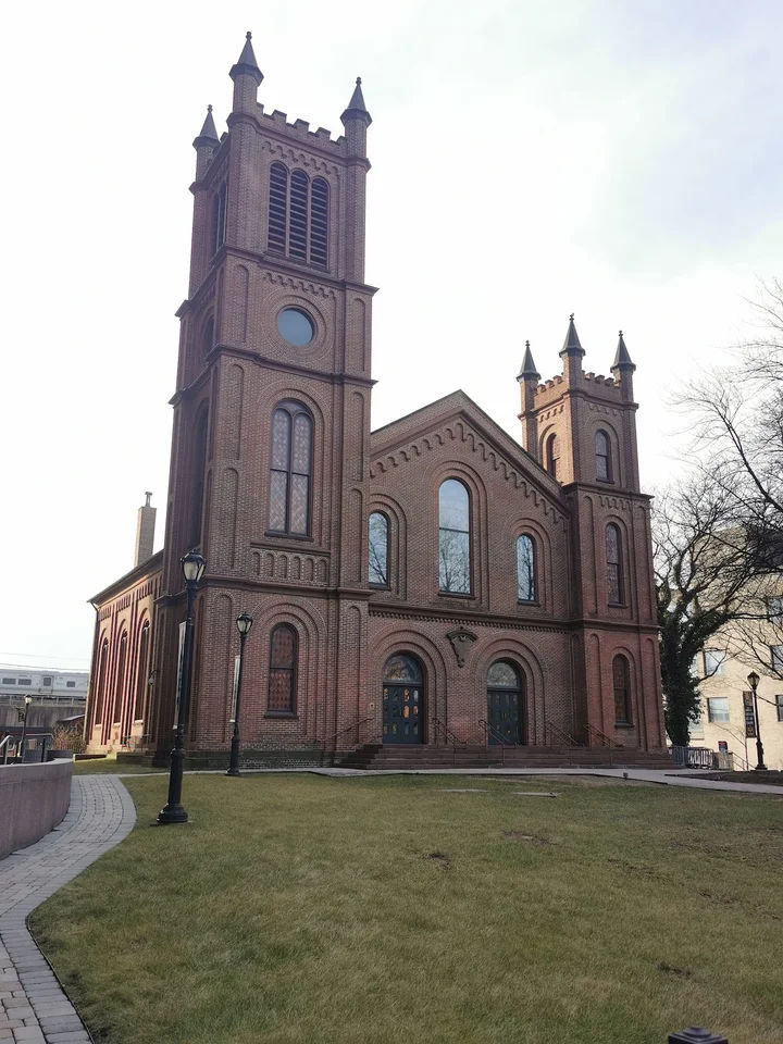First Presbyterian Church in Jamaica, Queens, New York, featuring its historic red-brick facade, twin towers, arched windows, and landscaped grounds.