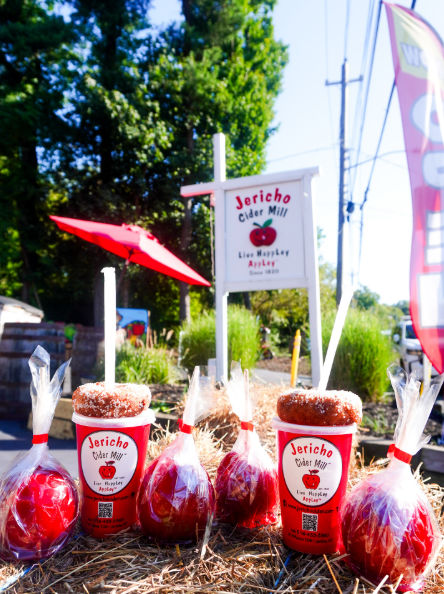 Freshly made candy apples and apple cider displayed outside Jericho Cider Mill in Jericho, New York. The seasonal display features red candy-coated apples, containers of cider, and the mill’s sign in the background, celebrating a longtime Long Island fall tradition.