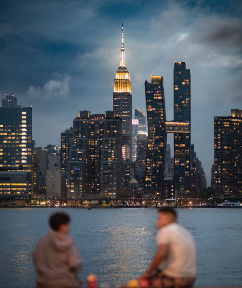 Sunset view from Gantry Plaza State Park in Long Island City, New York, showcasing the Manhattan skyline, the East River, historic gantry structures, and a waterfront promenade bathed in golden light.