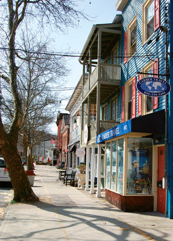 Street view in downtown Piermont, New York, featuring colorful storefronts, local businesses, outdoor seating, mature trees, and historic buildings lining the sidewalk.