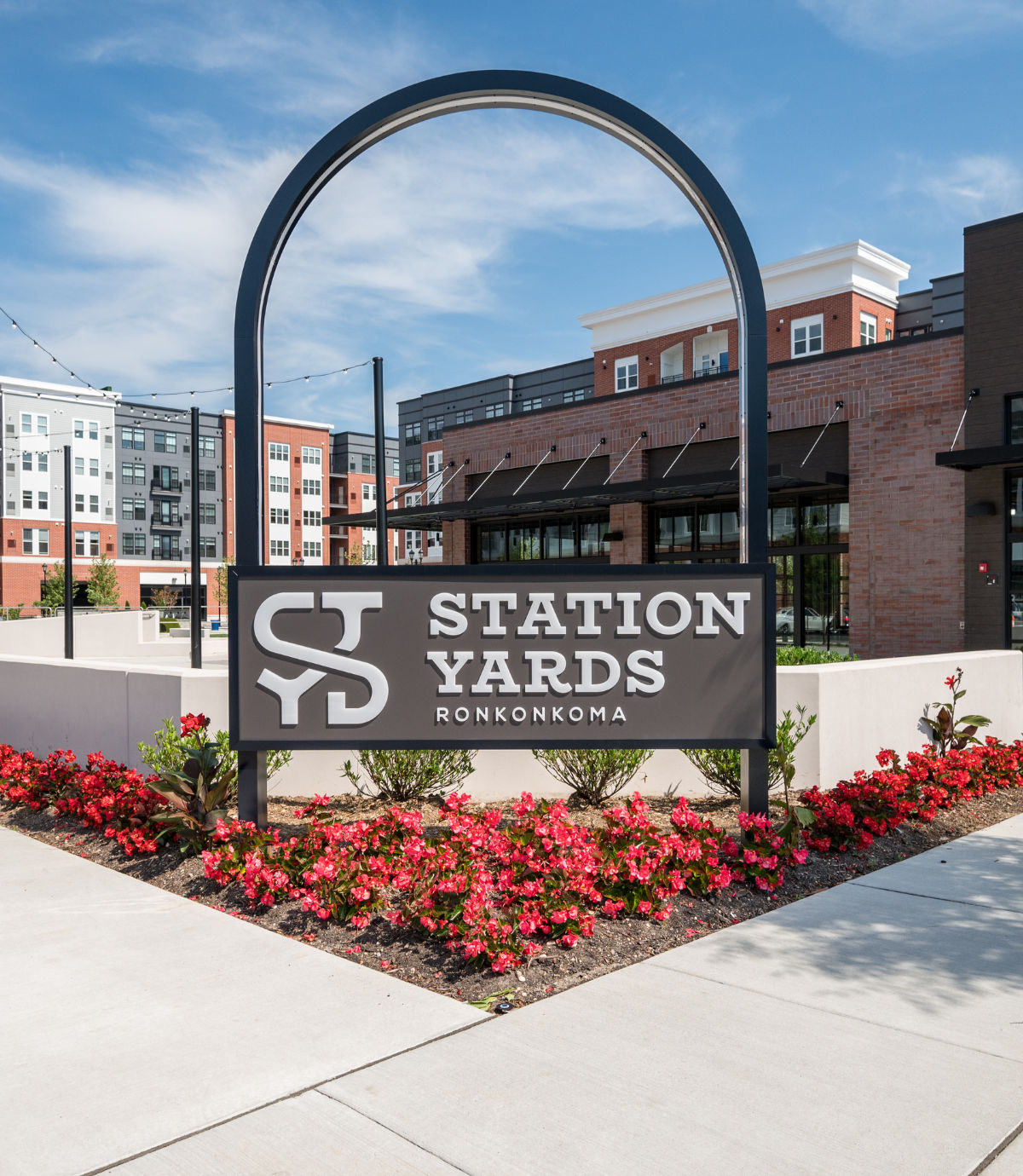 Entrance sign for Station Yards Ronkonkoma featuring modern apartment buildings, landscaped walkways, and a contemporary mixed-use development setting