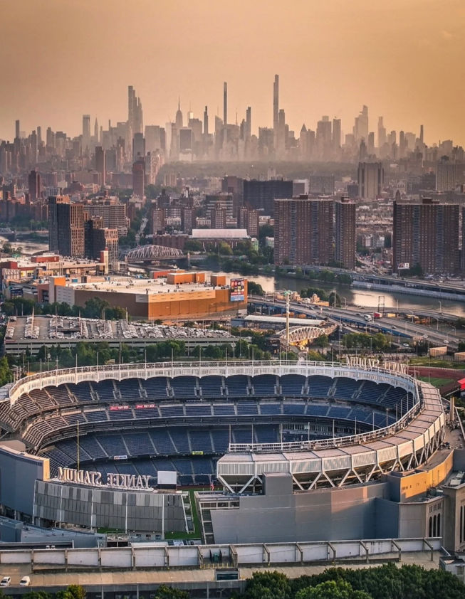 Yankee Stadium in the Bronx, New York, with the Harlem River, surrounding city neighborhoods, and Manhattan skyline in the distance.