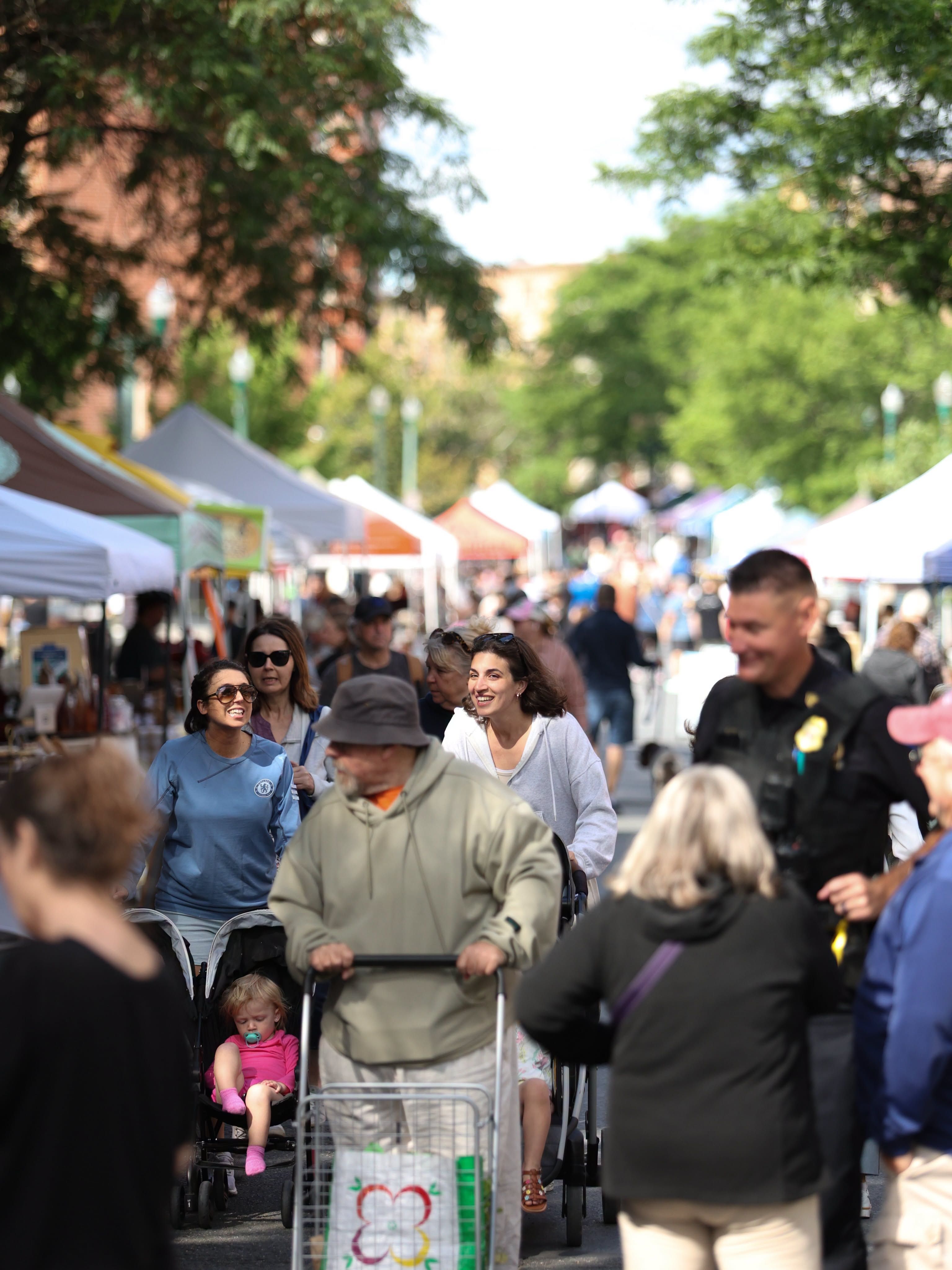 Shoppers exploring the Troy Waterfront Farmers Market in downtown Troy, New York, with local vendor tents, families, and community members enjoying the lively outdoor market.
