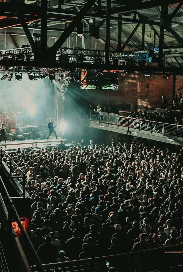 Crowded live music performance at The Paramount near Woodbury, New York, featuring a packed audience gathered inside a large indoor concert venue with stage lighting, balcony seating, and performers on stage during a nighttime show.