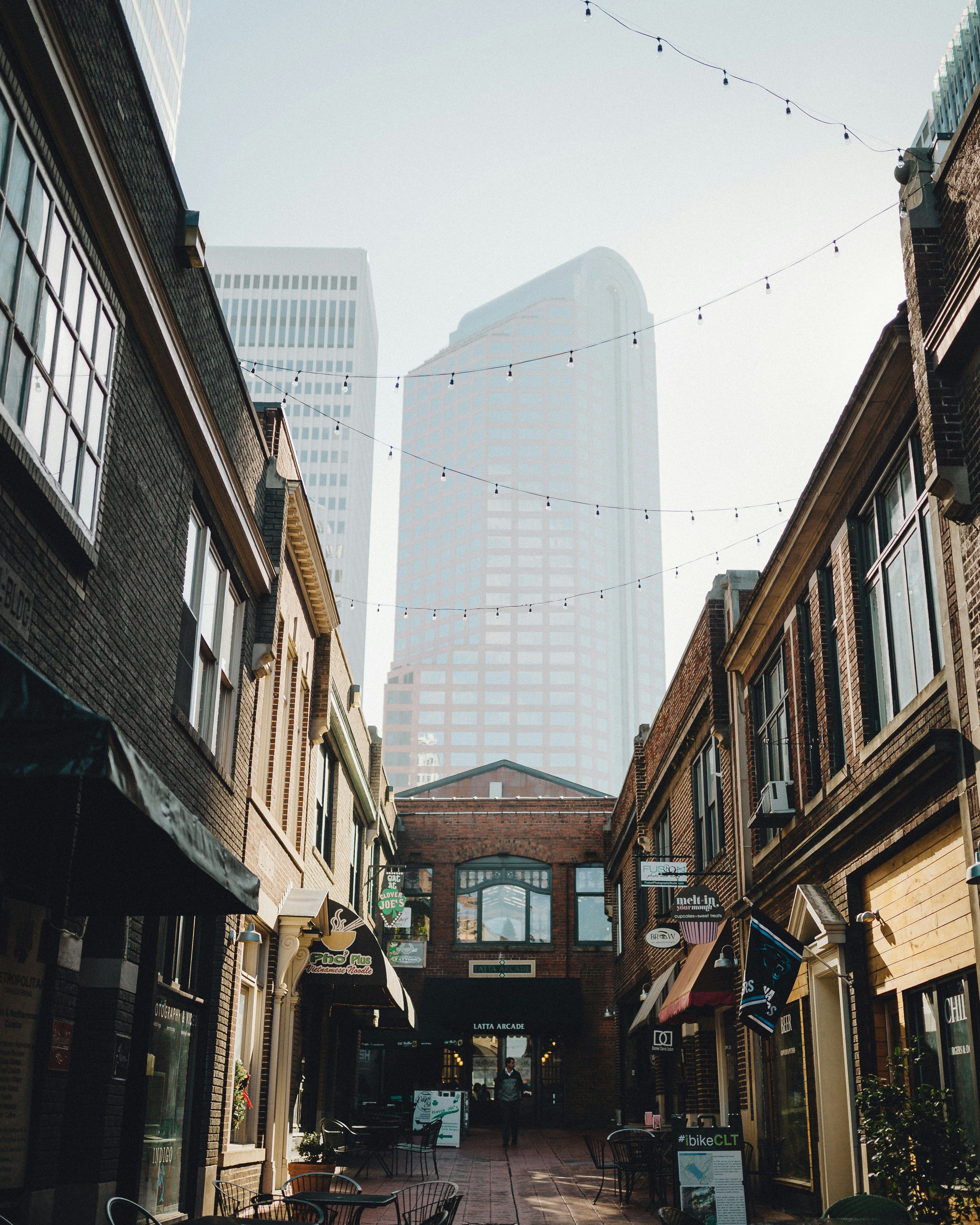 Charming brick-lined alleyway in Charlotte's NoDa or South End neighborhood with string lights and modern high-rise tower in the background