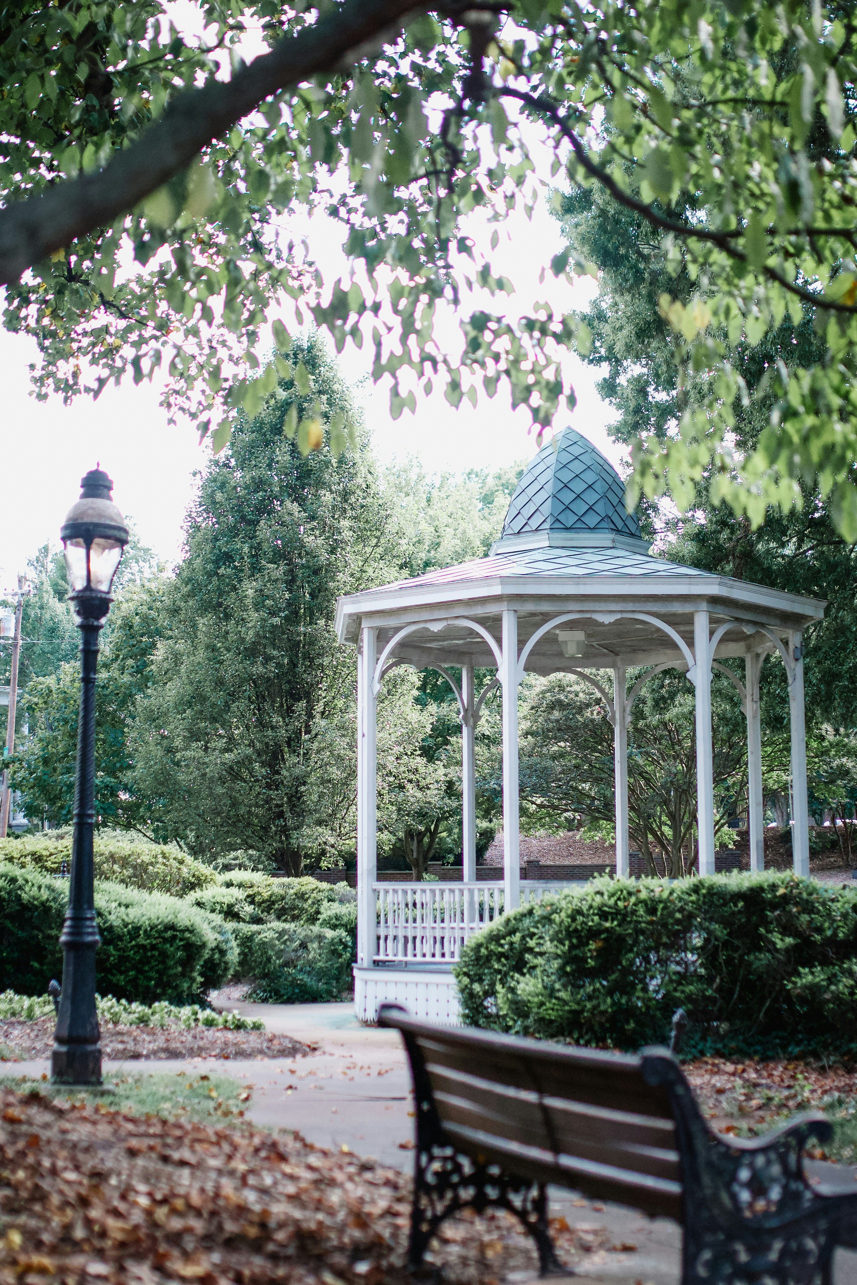 A charming white gazebo surrounded by lush green trees and blooming gardens in a peaceful park in Winston-Salem, North Carolina