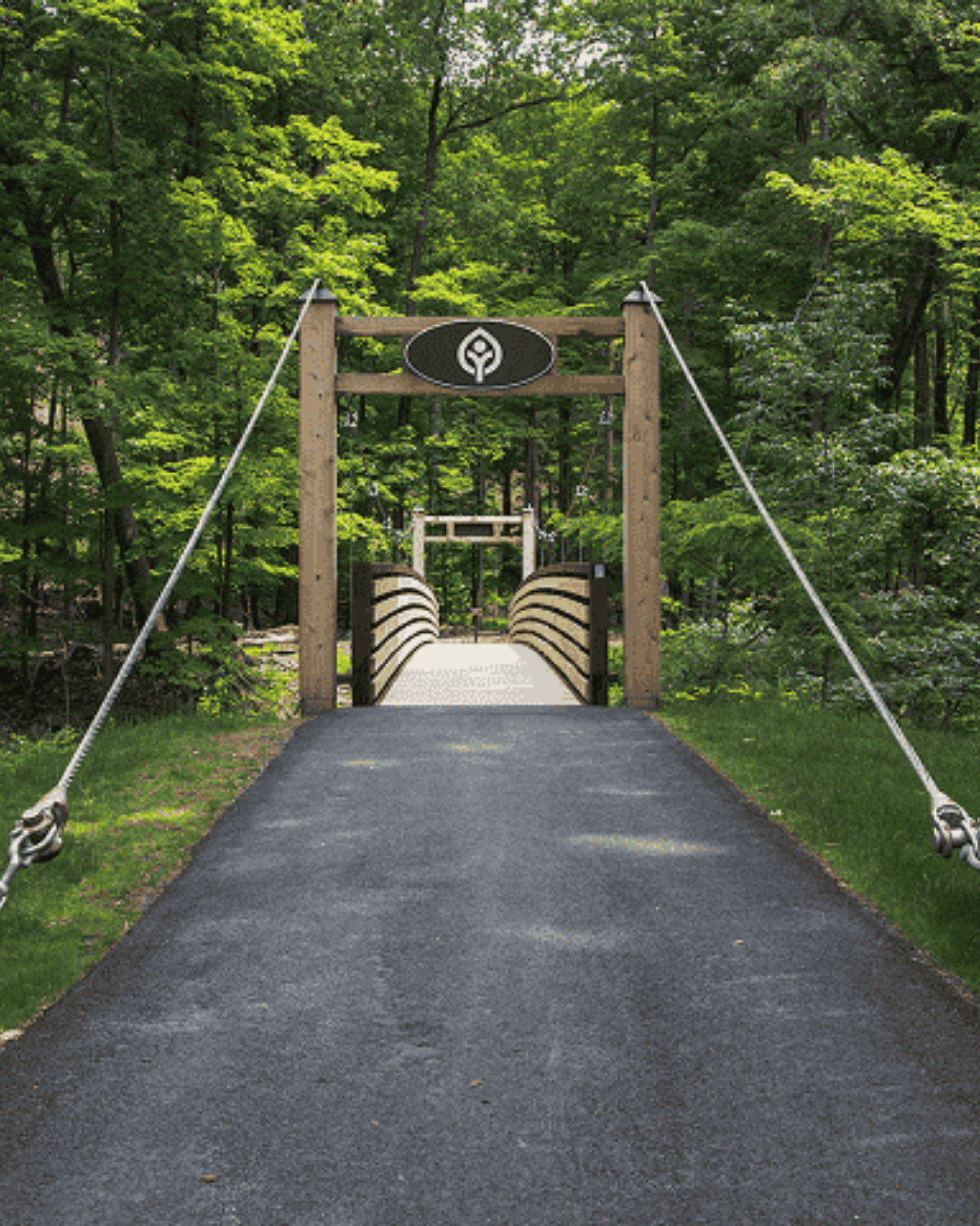 Paved trail and footbridge in Euclid Creek Reservation in Euclid, Ohio, with a park emblem sign mounted above the bridge