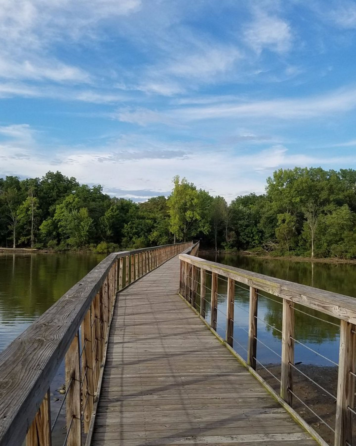 Scenic wooden boardwalk pier extending over a calm lake surrounded by lush green trees in Galena, Ohio