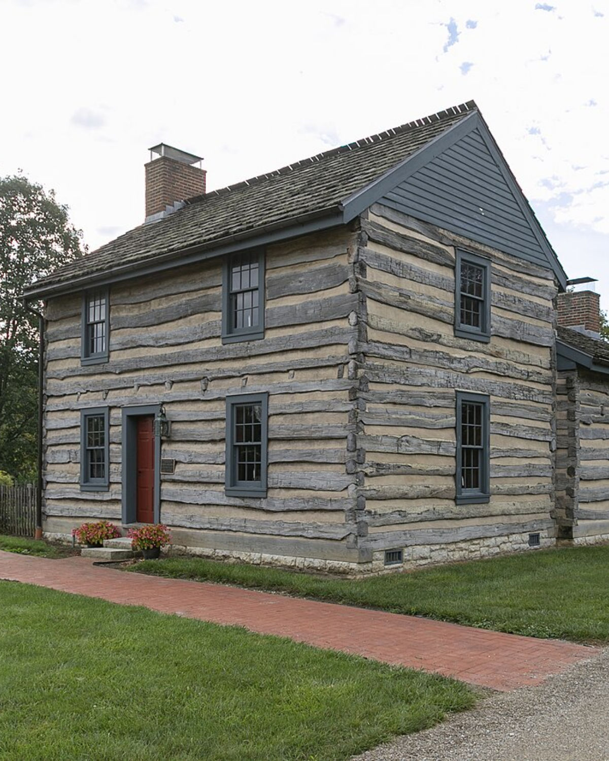 Historic hand-hewn log cabin with a red door and stone foundation in the preserved village of Historic Downtown Groveport, Ohio