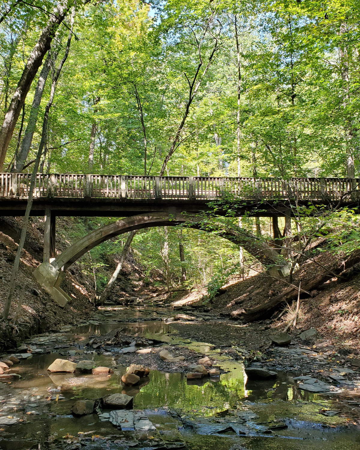 A rustic stone arch bridge spanning a wooded creek along a scenic nature trail in Powell, Ohio