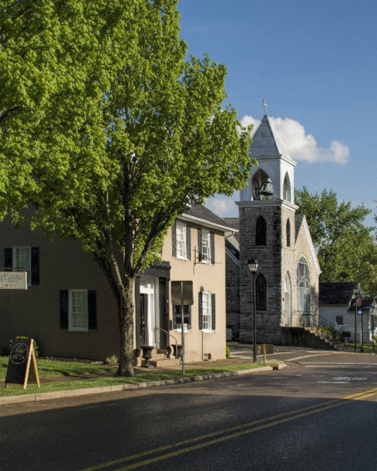 Historic stone church with a tall steeple on a tree-lined street in downtown Springboro, Ohio