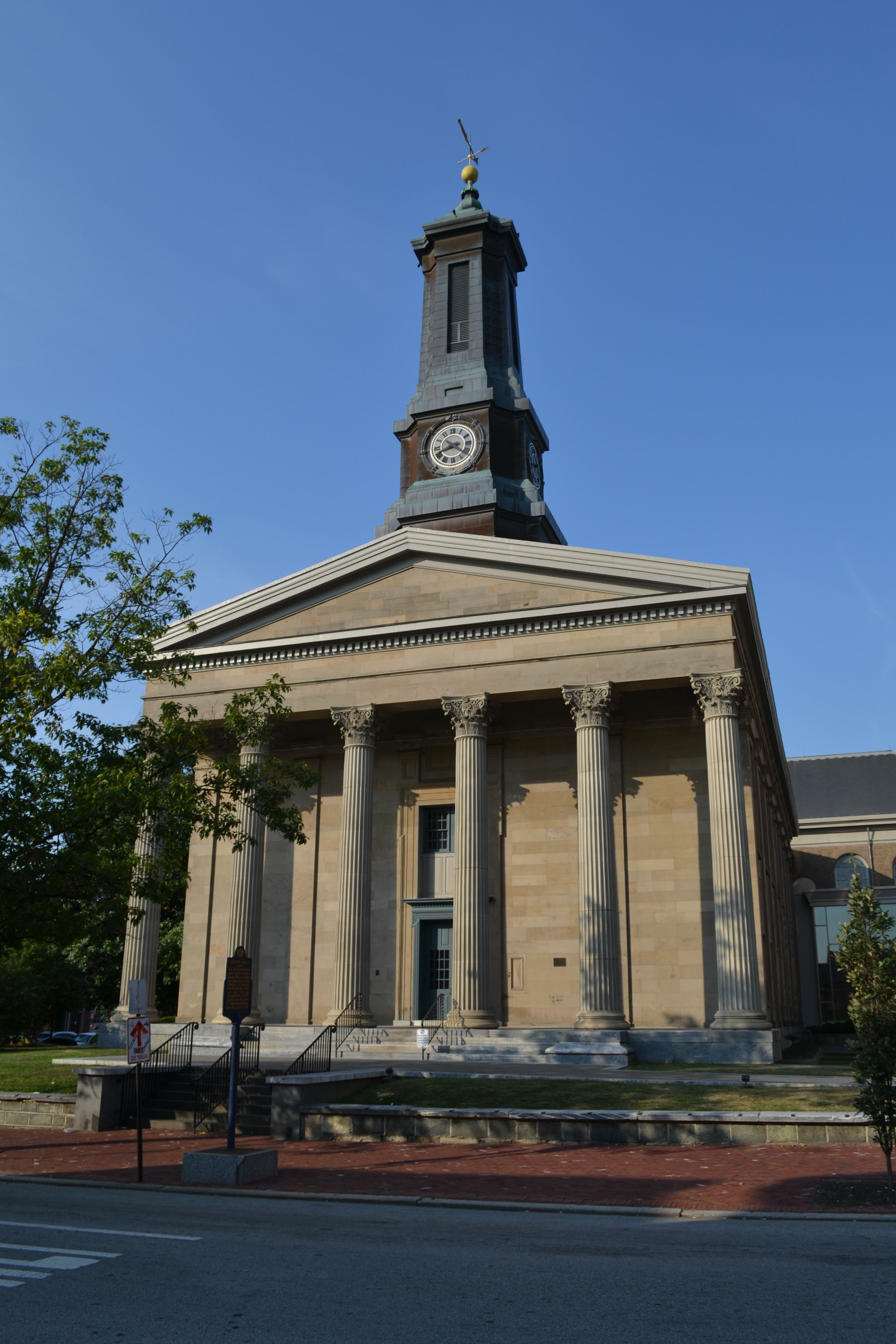 Front exterior of Chester City Hall, a neoclassical limestone building with tall Corinthian columns, a clock tower topped with a cupola, and broad steps leading to the main entrance beneath a clear blue sky.