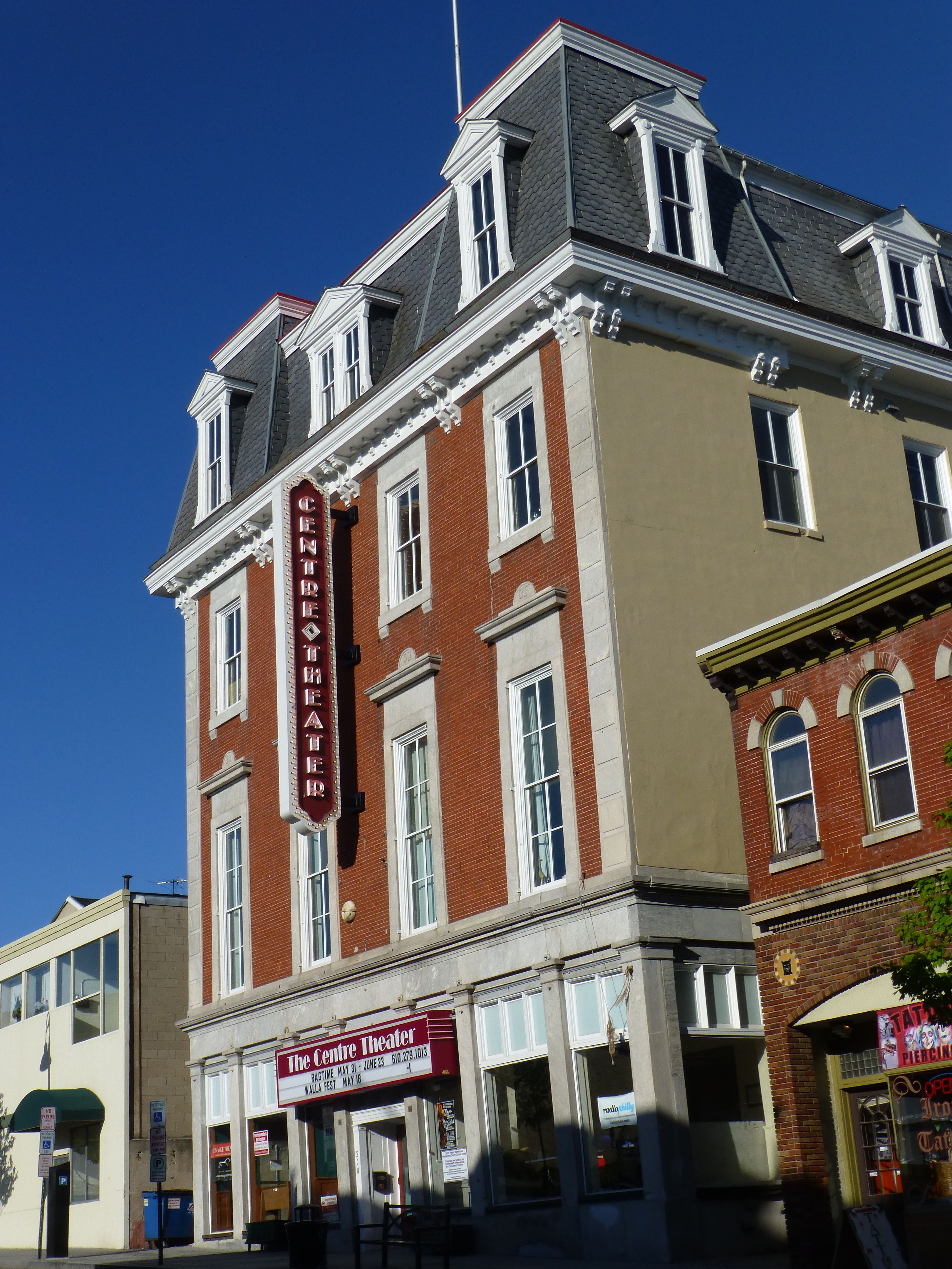 Front exterior of The Centre Theater in downtown Norristown, Pennsylvania, featuring a historic brick building with a mansard roof, vertical theater marquee, large front entrance, and neighboring storefronts along Main Street.