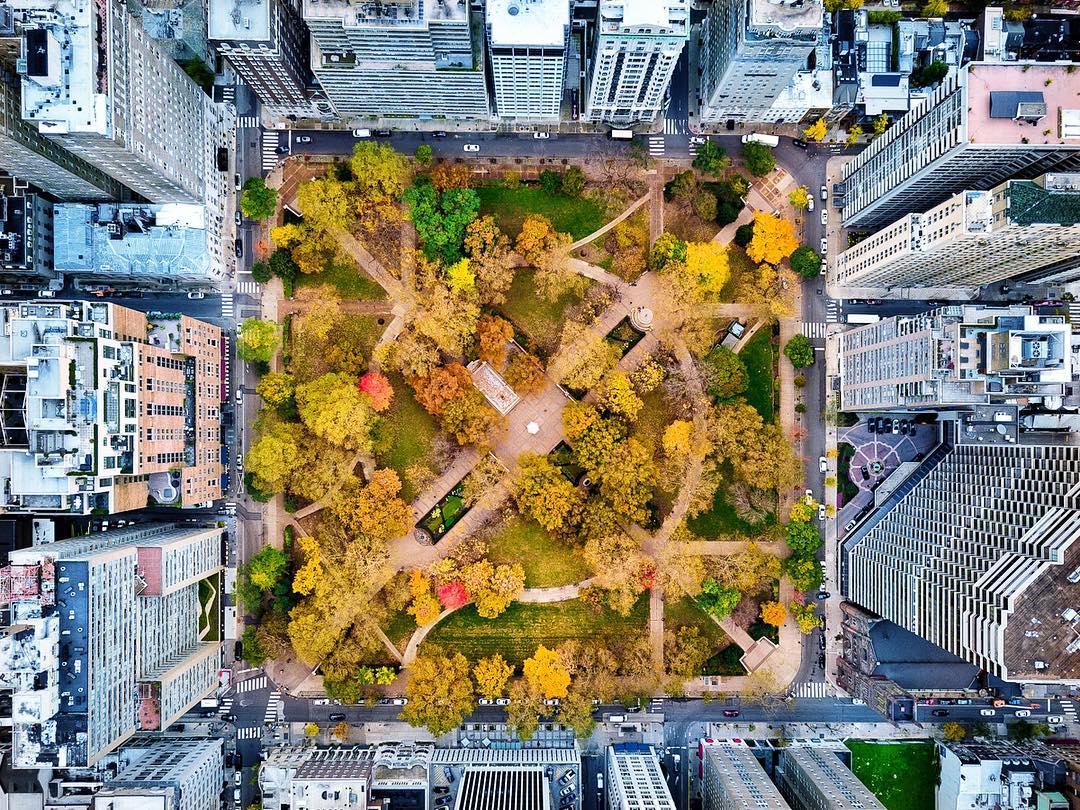 Aerial view of Rittenhouse Square in Philadelphia, Pennsylvania during fall, showcasing the park’s symmetrical walking paths, central plaza, and vibrant autumn foliage surrounded by dense city blocks, high-rise buildings, and streets lined with cars framing the square.