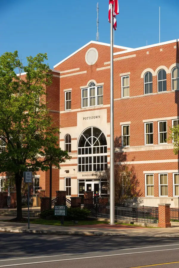 Front exterior of Pottstown Borough Hall in Pottstown, Pennsylvania, featuring a red brick civic building with arched windows, a central entrance, flagpole, and landscaped grounds along a downtown street.