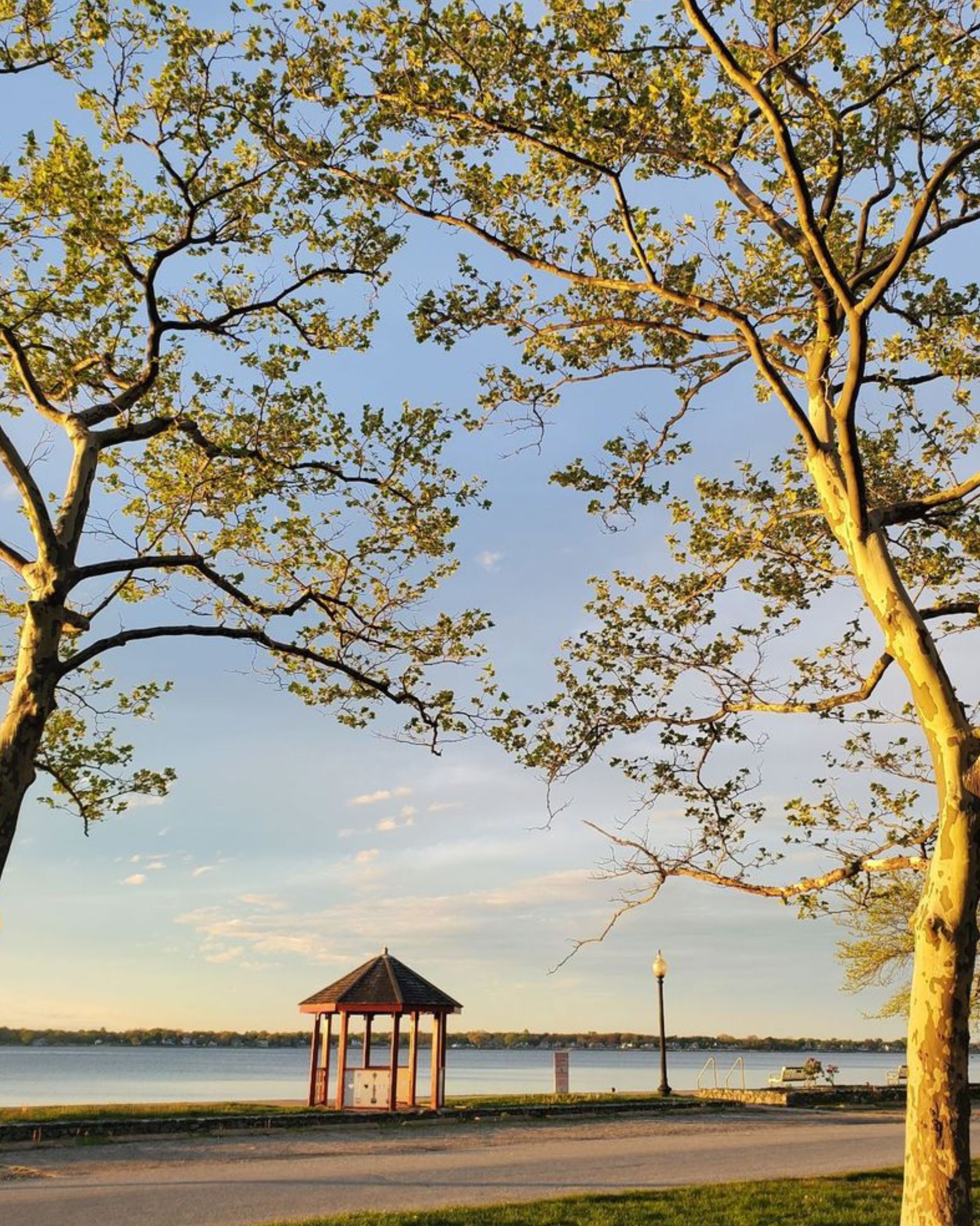 Golden-hour view of Goddard Memorial State Park in Warwick, Rhode Island, featuring a waterfront gazebo, mature shade trees, and scenic views of Greenwich Bay.