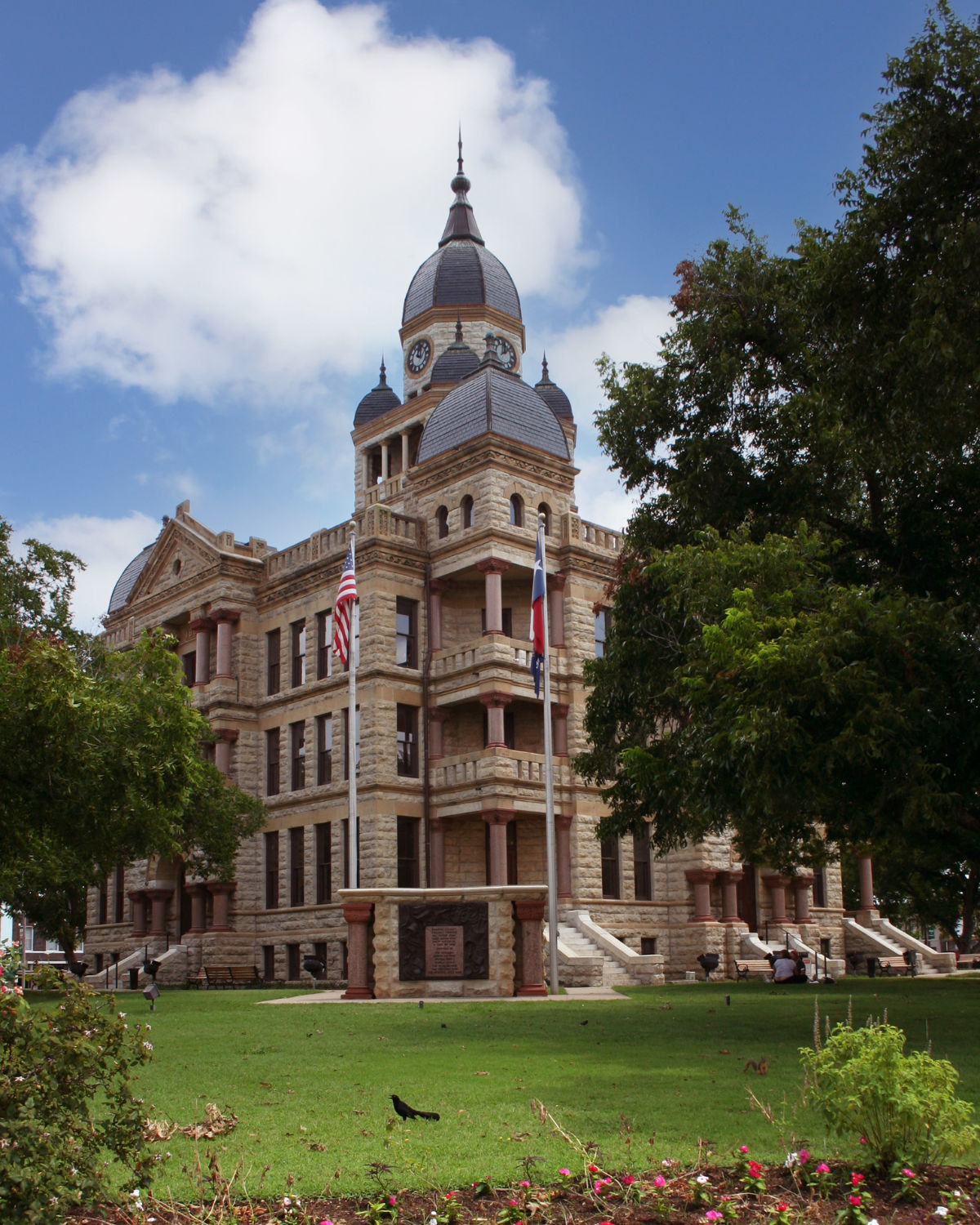 Historic Denton County Courthouse-on-the-Square in Denton, TX, a Victorian-era building with a clock tower and ornate stonework framed by mature trees