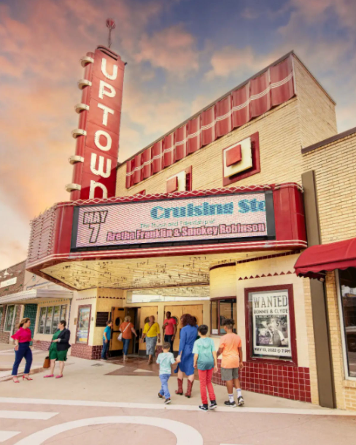 Historic Uptown Theater in Grand Prairie, Texas, with its retro red-and-cream marquee and vertical “Uptown” sign, as families and visitors walk toward the entrance under a pastel evening sky.