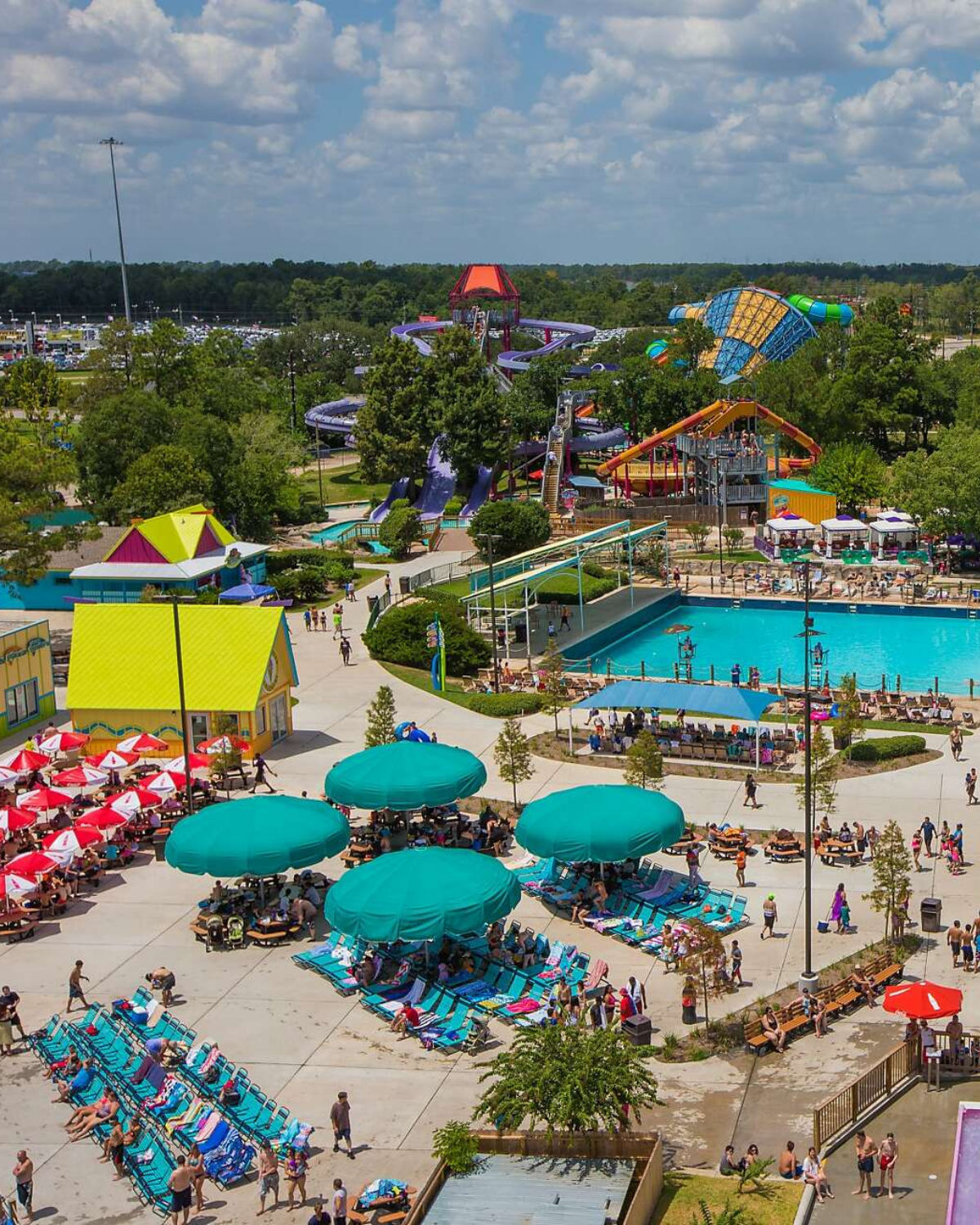 A bright aerial view of Six Flags Hurricane Harbor Splashtown in Spring, Texas, with colorful water slides, turquoise pools, and rows of lounge chairs and umbrellas filled with visitors enjoying a sunny day.