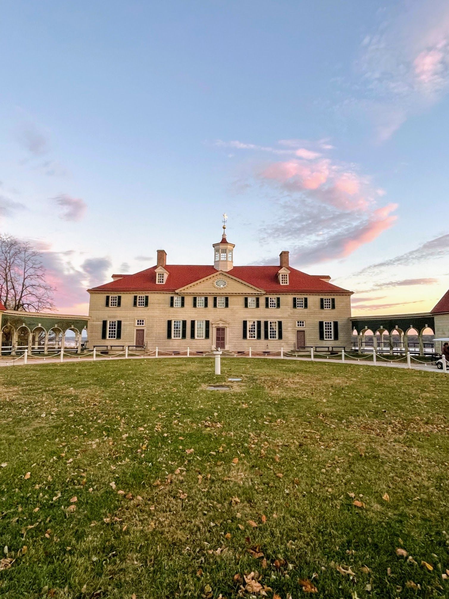 Front view of George Washington’s Mount Vernon estate in Alexandria, Virginia, featuring the historic mansion with a red roof, symmetrical architecture, and open lawn at sunset.