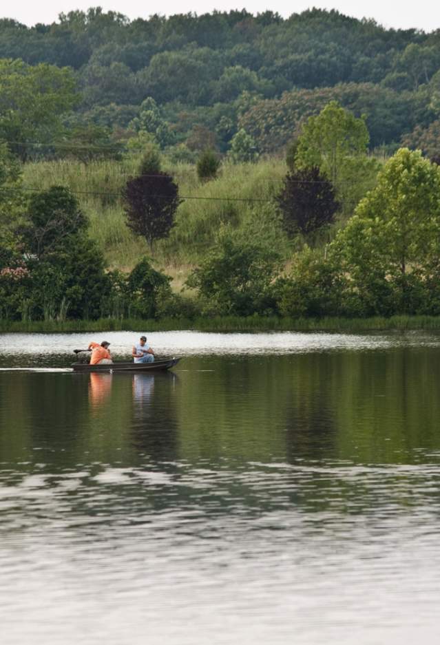 People fishing from a small boat on a peaceful lake in Haymarket, Virginia, surrounded by lush trees and scenic natural landscapes.