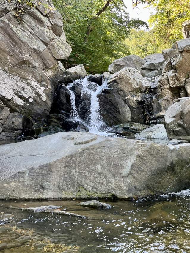 Small waterfall cascading over large rock formations in Scott's Run Nature Preserve near McLean, Virginia, surrounded by forest, natural pools, and rugged stone cliffs in a peaceful woodland setting.