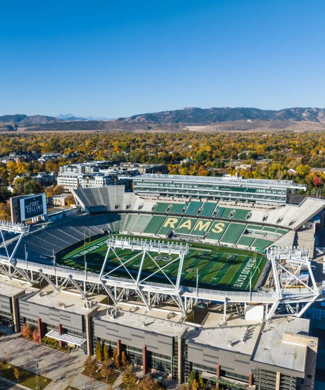 Aerial view of Canvas Stadium in Fort Collins, Colorado, home of the Colorado State Rams, set against a backdrop of fall foliage and the Rocky Mountain foothills.