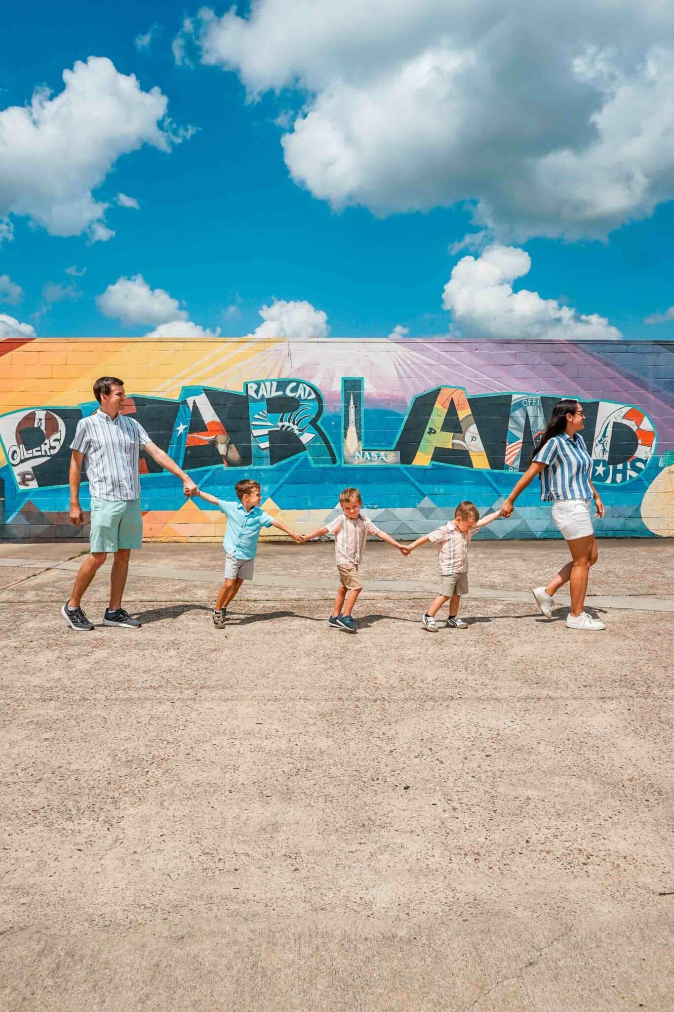 Family walking hand-in-hand in front of a colorful ÒPearlandÓ mural in Pearland, Texas, showcasing a bright, community-focused atmosphere under a clear blue sky.