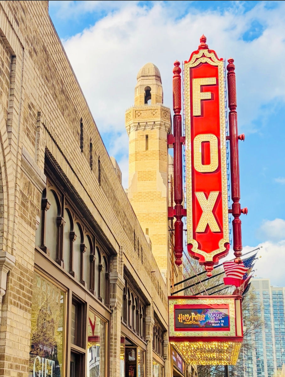 The historic Fox Performing Arts Center marquee in downtown Riverside, California, featuring a bright red vertical ÒFOXÓ sign against classic architecture and a lively city backdrop.
