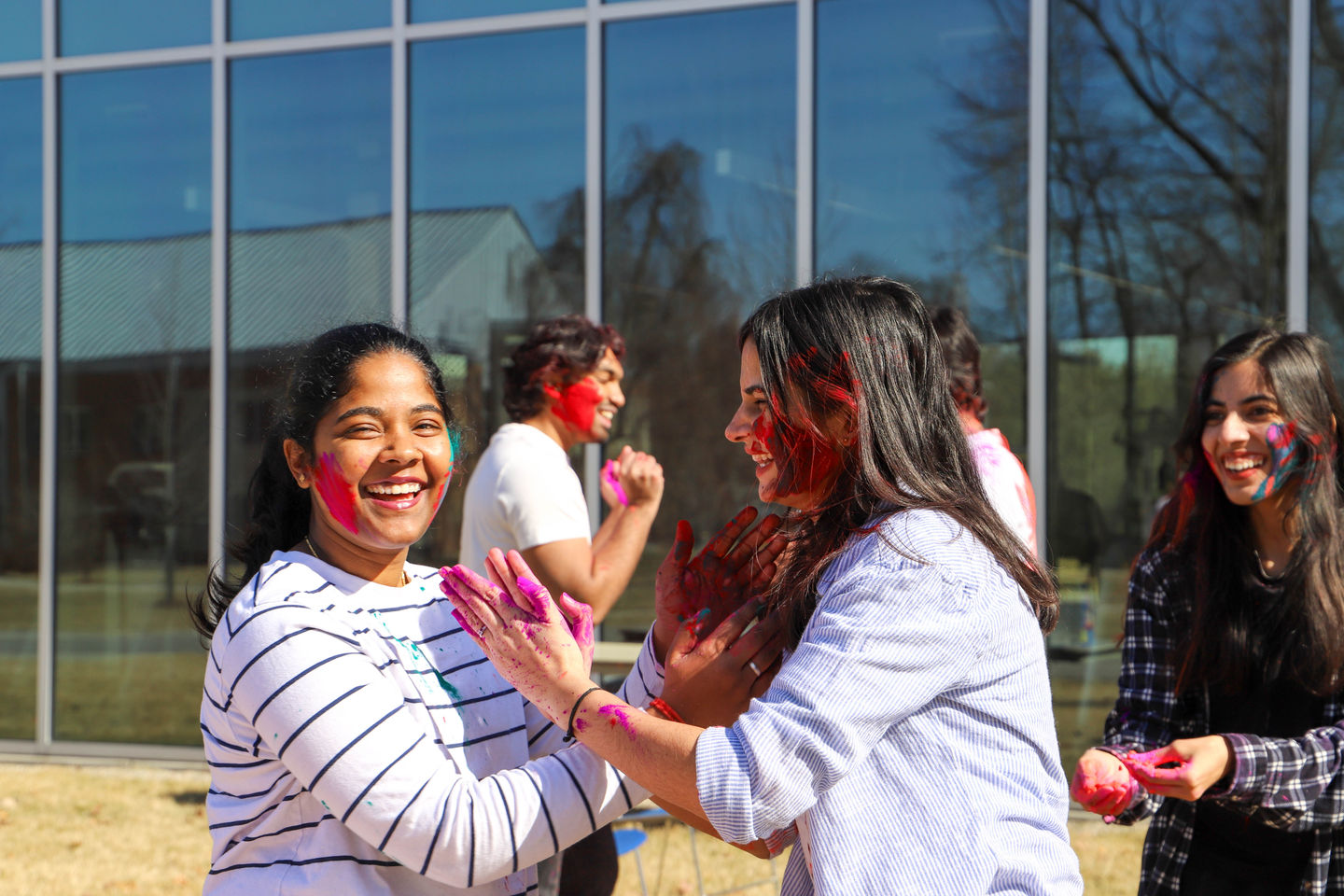 Smiling LTU Indian students covered in bright pink and red Holi powder celebrate outdoors on LTU's campus.