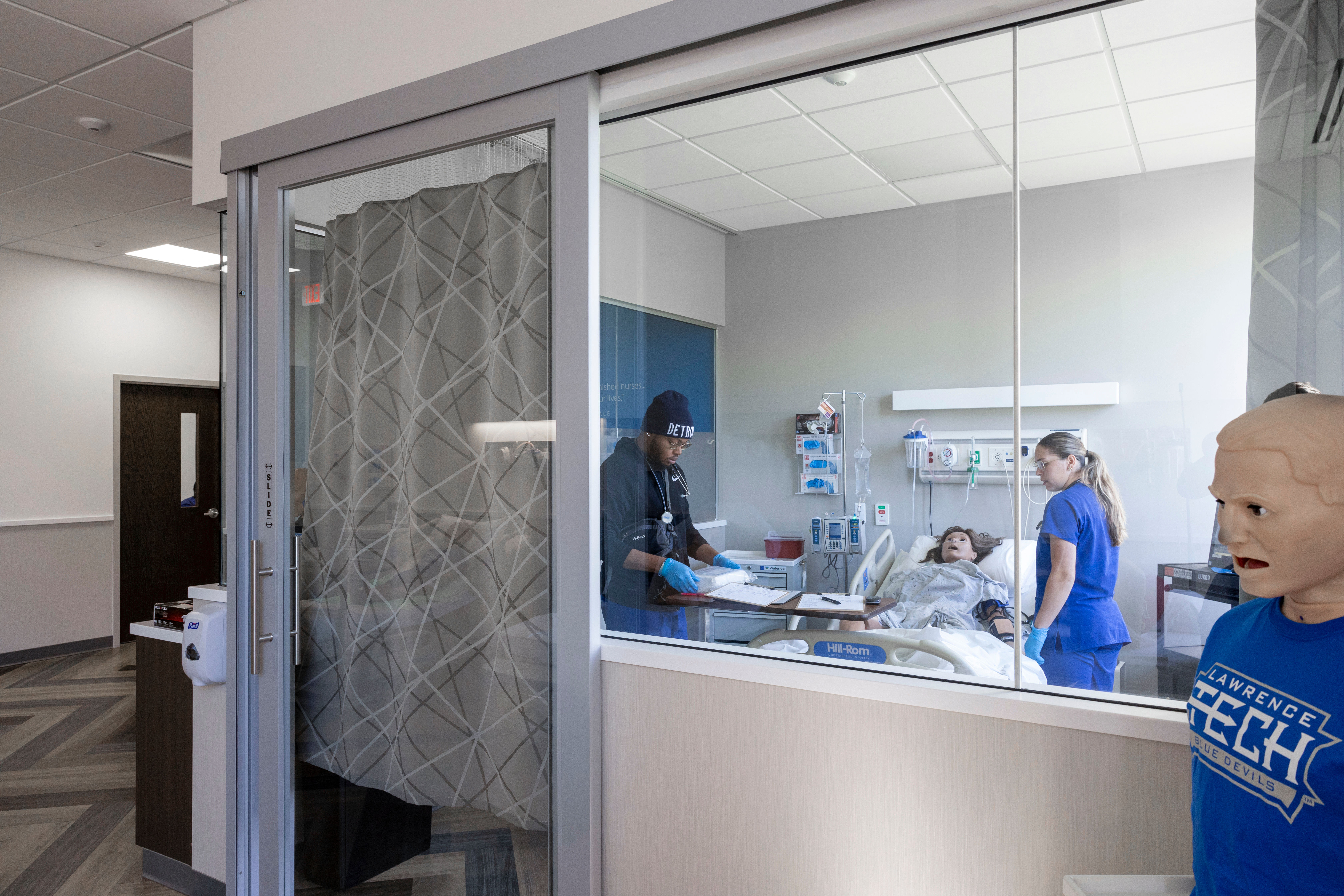 Lawrence Technological University Nursing students practice medical procedures on a patient simulator inside the LTU Sim Lab. A medical training mannequin visible in the foreground.