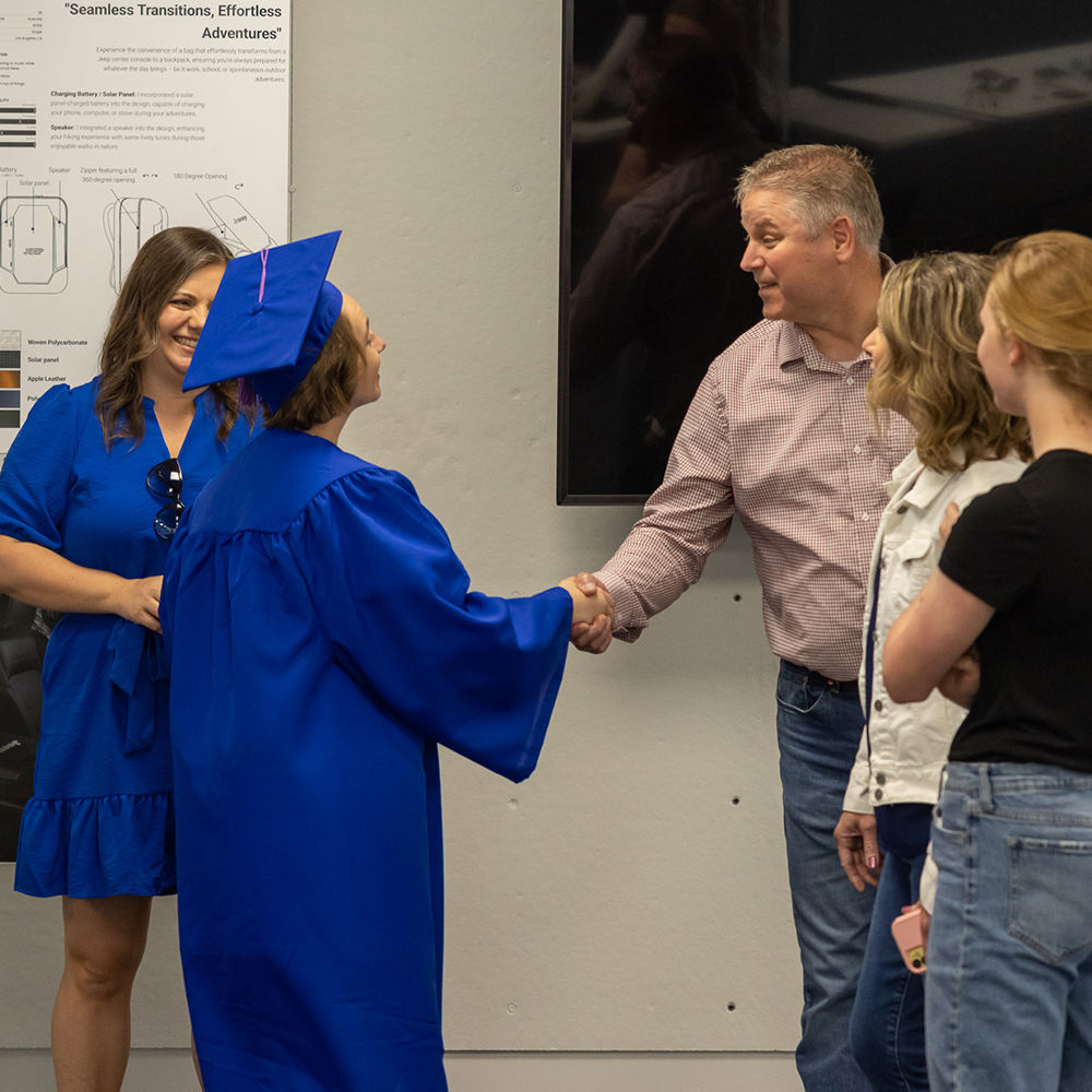 A graduate in an LTU-blue cap and gown shakes hands with an older man during the Show LTU CoAD family and friends celebration in the architecture building.