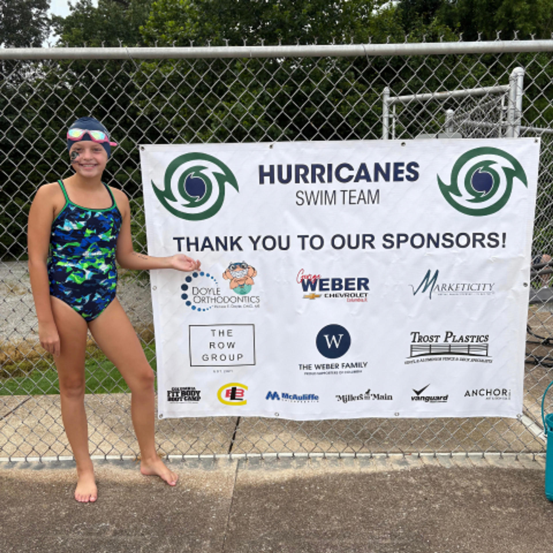 member of the hurricanes swim team posing in front of a sponsorship thank you banner
