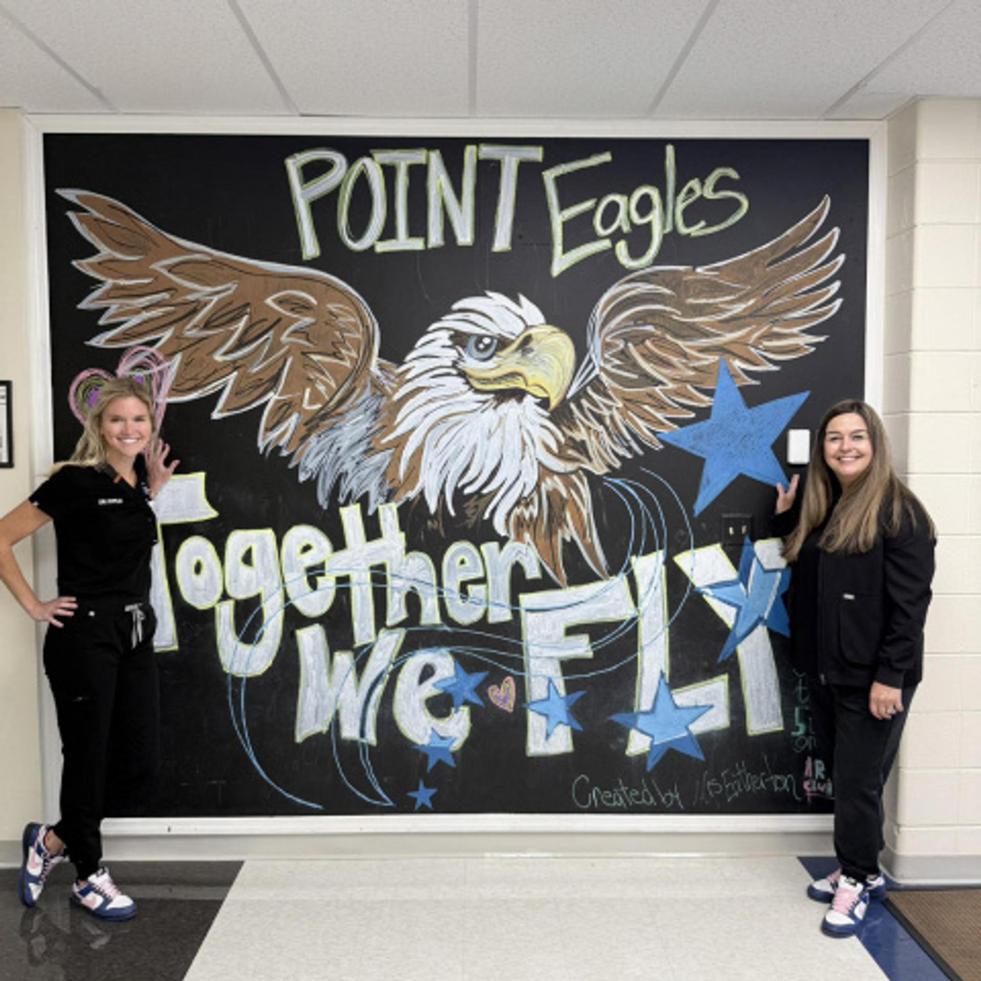 two Doyle employees in front of a large poster that reads Point Eagles Together We Fly